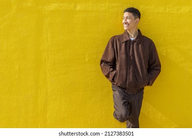 Happy guy smiling looking to the left. Yellow wall background. Latin 18-20 years old guy. Outdoor portrait