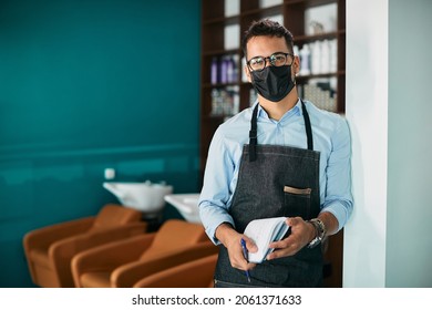 Happy Hairdresser Wearing Face Mask While Working At Hair Salon During Coronavirus Pandemic And Looking At Camera.