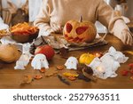 Happy Halloween! Carving halloween pumpkin. Woman holding pumpkin and knife on table with ghosts and spiders. Making halloween decorations