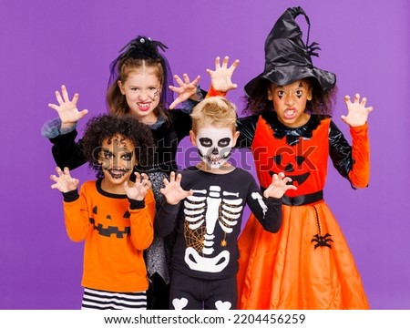 Happy Halloween! Cheerful kids in carnival costumes and makeup make a terrible gesture on bright colored purple background