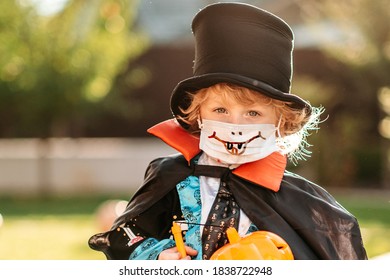 Happy Halloween. A Child In A Medical Mask In A Dracula Costume Sits On A Pumpkin In His Yard.