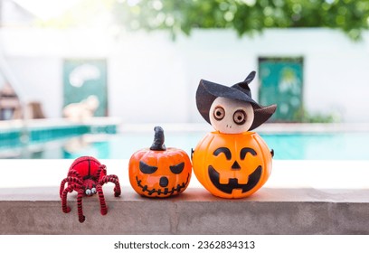 Happy Halloween concept background, outdoor day light, wooden with doll in Halloween pumpkin lantern and red yarn spider on swimming pool edge, tropical style