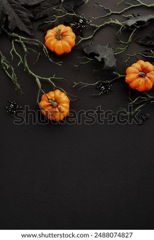 Happy Halloween concept. Flat lay bright orange pumpkins, branches with bats, dark leaves, and creepy spiders on black background. Perfect for seasonal content, evoking the spooky spirit of Halloween