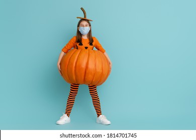 Happy Halloween! Cute Little Girl In Pumpkin Costume  Wearing Face Mask Protecting From COVID-19.