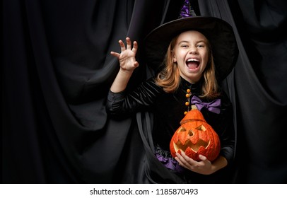 Happy Halloween! Cute Little Laughing Girl In Witch Costume On Black Wall Background. 