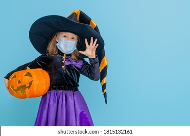 Happy Halloween! Cute little witch with a pumpkin  wearing face mask protecting from COVID-19.