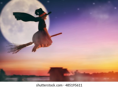 Happy Halloween! Cute little witch flying on a broomstick. Beautiful young child girl in witch costume outdoors. 
