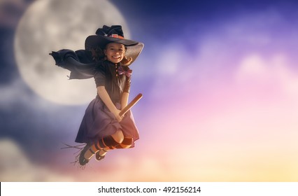 Happy Halloween! Cute Little Witch Flying On A Broomstick. Beautiful Young Child Girl In Witch Costume Outdoors. 