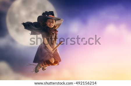 Happy Halloween! Cute little witch flying on a broomstick. Beautiful young child girl in witch costume outdoors. 