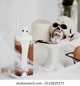 Happy Halloween. A fancy ghost Halloween Drink Iced chocolate with cute ghost made from marshmallow. A white candle and skull on blurry background. Spider web on foreground. White Halloween party. - Powered by Shutterstock