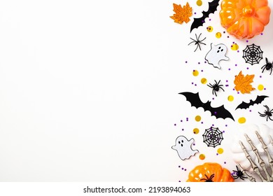 Happy Halloween flat lay composition with pumpkins, bats, ghosts, skeleton arms, spiders, webs. Top view, copy space. Halloween holiday greeting card mockup.