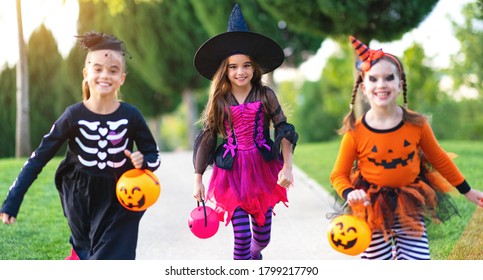 Happy Halloween! Funny Kids Girls Laughing In Fancy Dress With Bucket Run Laughing Along The Path In The Garden Outdoor
