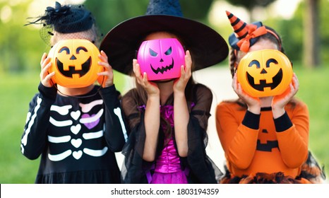 Happy Halloween! Funny Kids Girls   In Fancy Dress Hide Their Heads Behind Buckets Pumpkins Outdoors
