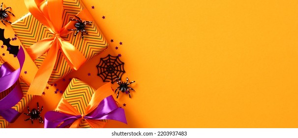 Happy Halloween holiday banner design. Flat lay gift boxes, spiders, bats, confetti on orange background. Top view with copy space.