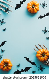 Happy Halloween holiday concept. Frame made of pumpkins, skeleton hands, bats, spiders on blue background. Flat lay, top view, overhead.