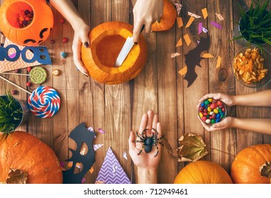 Happy halloween! A mother, father and their daughter carving pumpkin on the table in the home. Family preparing for holiday. Top view. Close up. - Shutterstock ID 712949461