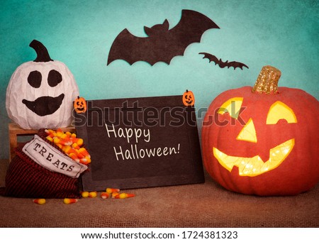 Happy Halloween Pumpkin Still Life Scene with sign board with text, ghost gourd, treats bag, against teal background with bats flying.  A horizontal photo with texture treatment.