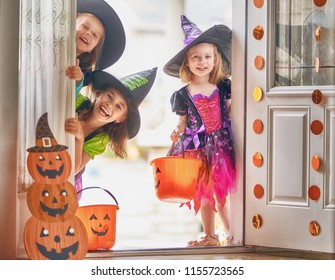 Happy Halloween! Three Cute Little Laughing Girls In Witches Costumes Are Coming To The House For Sweets.