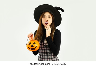Happy halloween, young asian woman in black costume wearing witch hat carrying lantern pumkin posing exciting on white background.