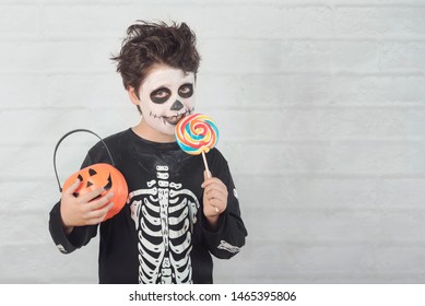 Happy Halloween.funny Child In A Skeleton Costume Eating Lollipop In Halloween Against 
Brick Background