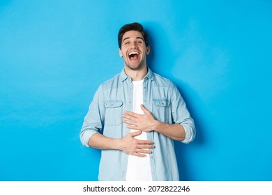 Happy Handsome 30 Year Old Man Touching Belly, Laughing Out Loud And Looking At Something Funny, Standing Against Blue Background