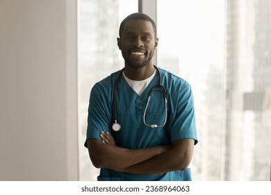 Happy handsome African American surgeon in blue scrubs standing indoors with arms crossed on chest, looking at camera with toothy smile. Positive male doctor headshot portrait - Powered by Shutterstock