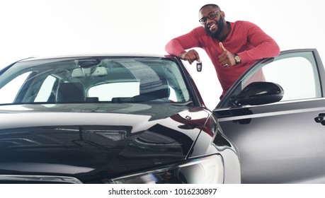 Happy Handsome African Man Showing Car Keys In Near His Newly Bought Vehicle Car Smiling Cheerfully Copy Space Owner Ownership Sales Driving Consumerism Private Taxi Concept Studio Shot