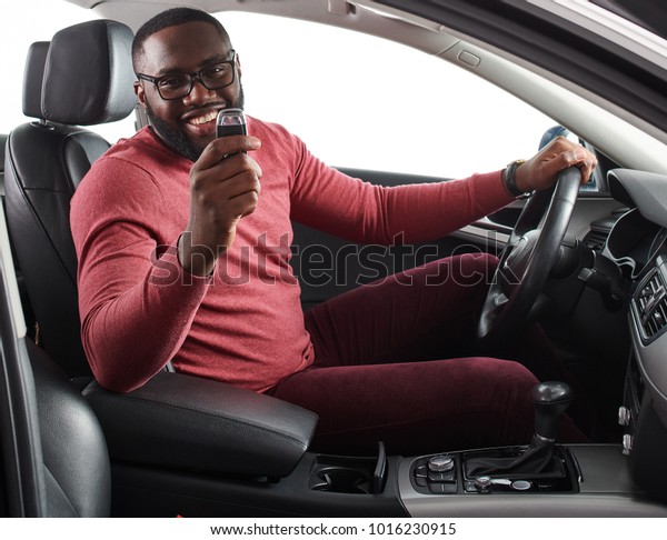 Happy handsome African man showing car keys in\
his newly bought auto smiling cheerfully sitting in the  luxury\
vehicle copy space owner ownership sales driving consumerism\
private taxi concept
