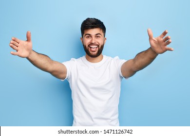 happy handsome Arab bearded young man standing with raised arms, he wants to hug his friend, isolated on blue background.. I love you. I miss you.body language