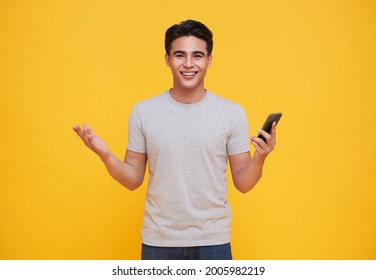 Happy Handsome Asian Man Celebrating With Mobile Phone Isolated Over Yellow Background.