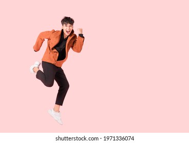 Happy handsome Asian man in fashionable clothing and jumping doing winner gesture isolated on pink background with clipping path. Portrait of young male cheerful jumping in air and smiling in studio. - Shutterstock ID 1971336074