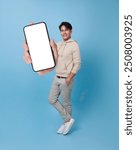 Happy handsome Asian man showing smartphone mockup of blank screen isolated on blue background.