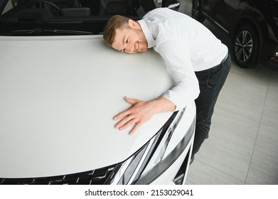 Happy Handsome Bearded Man Buying A Car In Dealership, Guy Hugging Hood Of New Car.