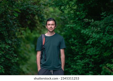 Happy Handsome beautiful man  30 years standing on road  forest green  shirt caucasian trees background outdoors nature park summer beard smiling happy casual backpack hands in pocket. - Powered by Shutterstock