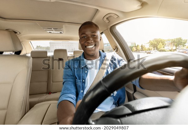 Happy handsome black guy driving his new car,\
going to office or travelling, copy space. Smiling african american\
young man sitting in comfortable auto, having car trip alone, shot\
from dashboard