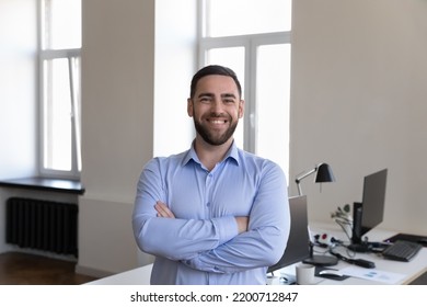 Happy handsome businessman looking at camera, smiling posing with folded hands at office workplace desk. Business startup leader man, CEO, confident professional head shot portrait - Powered by Shutterstock