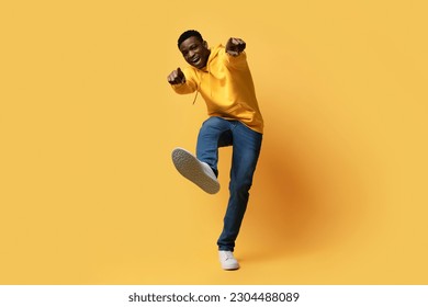 Happy handsome curly young black man in stylish casual outfit showing thumb ups and shoe sneaker sole on yellow studio background, like something or someone, copy space. Human gestures concept - Powered by Shutterstock