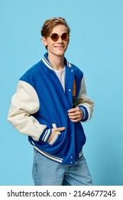 a happy, handsome, fashionable student in a blue bomber jacket is standing in sunglasses and with a bright backpack on his back. Vertical studio photography - Shutterstock ID 2164677245