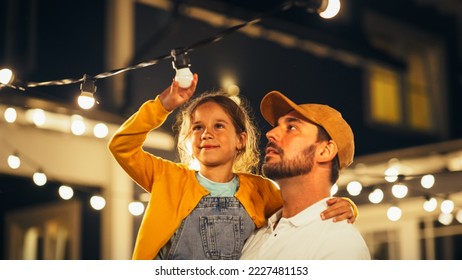 Happy Handsome Father Helping His Little Beautiful Daughter to Change a Lightbulb in Fairy Lights Backyard Installation at Home. Father and Daughter Repair Lights on a Porch.