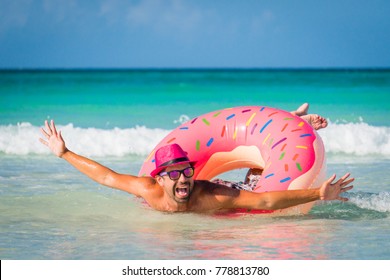 Happy handsome funny smiling man in pink hat swims on big inflatable tube at the coast of Caribbean Sea in summer sunny day