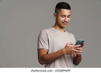 Happy handsome guy using mobile phone and smiling isolated over grey background
