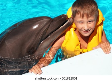 Happy handsome little boy smiling and swimming with dolphin in the blue swimming pool