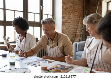Happy handsome man in apron drawing picture with paints on paper, enjoying creative art master class workshop with smiling multiracial young and old people, sitting together at table in loft studio. - Powered by Shutterstock