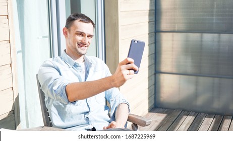 Happy Handsome Man Having A Facetime Video Call Talking To His Family. Smiling Man Taking Smelfies Outside On A Sunny Day. Self Isolation At Home On Balcony. 