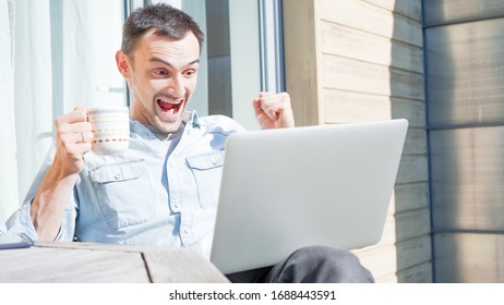 Happy Handsome Man Having A Facetime Video Call Talking To His Family. Laughing  During A Video Conference Outside On A Sunny Day. Self Isolating At Home On Balcony Drinking Coffee. 