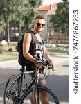 Happy handsome man hipster with sunglasses in tank top stands near a bicycle and having fun in the city on a sunny day