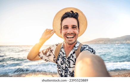 Happy handsome man taking selfie pic with cellphone outside - Male tourist enjoying summer vacation at beach holiday - Travel life style concept with smiling guy laughing at camera - Powered by Shutterstock