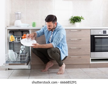 Happy handsome man unloading dishwasher and enjoying in housework. Husband doing chores in kitchen - Powered by Shutterstock