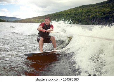 Happy handsome man wakesurfing in a lake and pulled by a boat. - Powered by Shutterstock