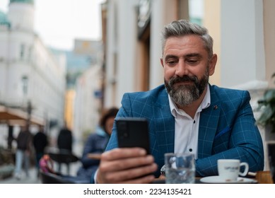 A happy handsome mature business man typing on his phone at a restaurant cafe during a coffee break. - Powered by Shutterstock